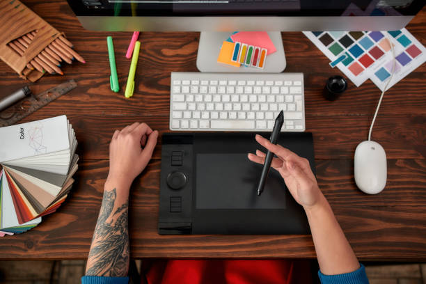 istock Making creative design. Top view of male hands using digital graphics tablet and desktop in the office or studio. Workplace with graphic tablet, keyboard, computer and color swatches 1209750938
