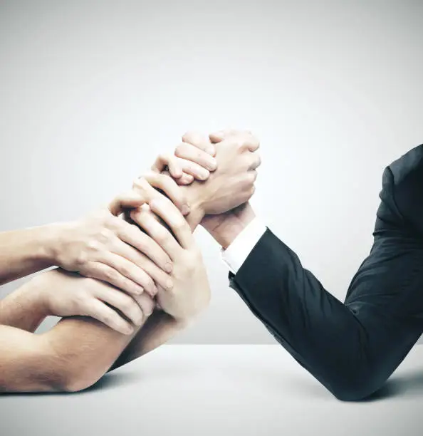 Businessman in opposition with many hands on gray background. Arm wrestling and business challenge concept