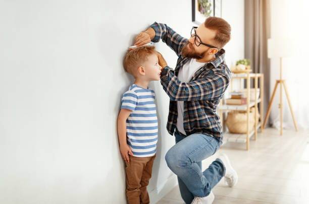 concepto de desarrollo, creciendo. padre mide la altura de su hijo pequeño - corto longitud fotografías e imágenes de stock