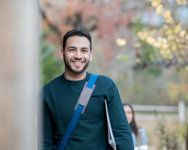 istock Male adult student smiles while leaning against wall while on campus 1209763603