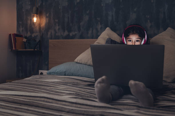 istock little girl sitting on the bed with a computer 1209764346