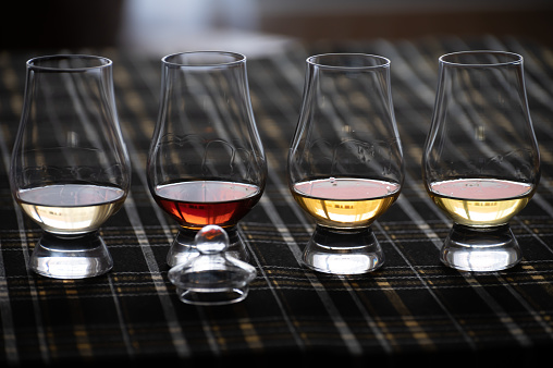 Four Special tulip-shaped glasses for tasting of Scotch whisky on distillery in Scotland, UK and dark tartan close up