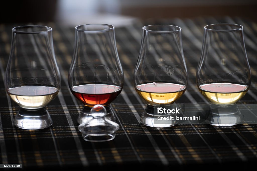 Four Special tulip-shaped glasses for tasting of Scotch whisky on distillery in Scotland, UK and dark tartan Four Special tulip-shaped glasses for tasting of Scotch whisky on distillery in Scotland, UK and dark tartan close up Whiskey Stock Photo