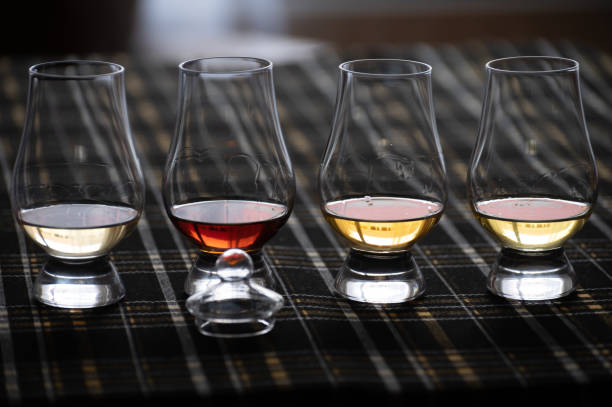 Four Special tulip-shaped glasses for tasting of Scotch whisky on distillery in Scotland, UK and dark tartan Four Special tulip-shaped glasses for tasting of Scotch whisky on distillery in Scotland, UK and dark tartan close up distillation photos stock pictures, royalty-free photos & images