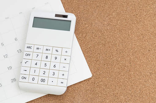 Flat lay or top view of white calculator on calendar on wooden background with copy space, tax schedule time, year or monthly financial expense, cost or investment planning.