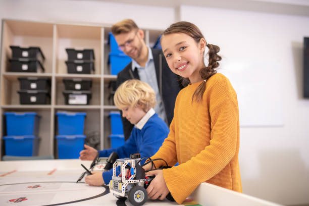 istock Dark-haired girl holding buildable car, boy playing with his, teacher watching them 1209797762
