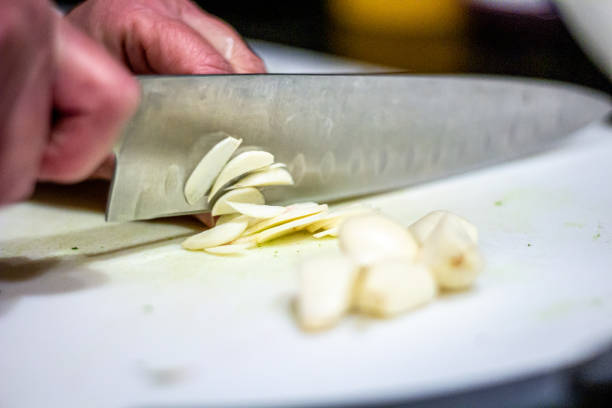 istock Caucasian Hand Chopping Freshly Peeled Garlic With a Silver Kitchen Knife on a Plastic White Cutting Board for Dinner Prep 1209800466