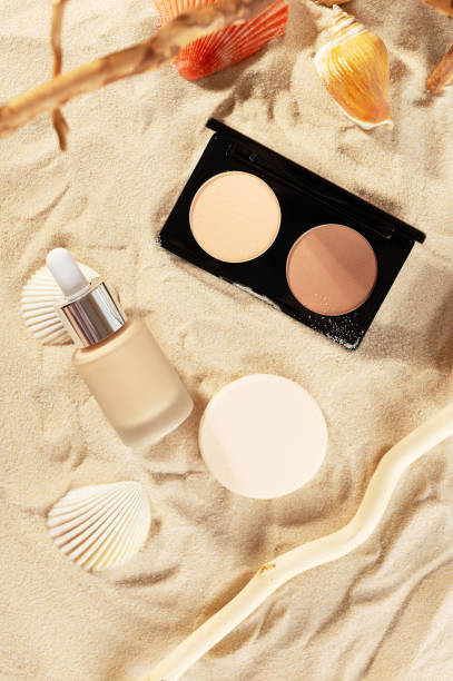 kit de cosméticos de verão facial. pó de contorno, creme líquido de fundação e esponjas de algodão na areia dourada com cascas de fundo. maquiagem profissional e conceito de beleza - make up foundation cosmetics face powder - fotografias e filmes do acervo