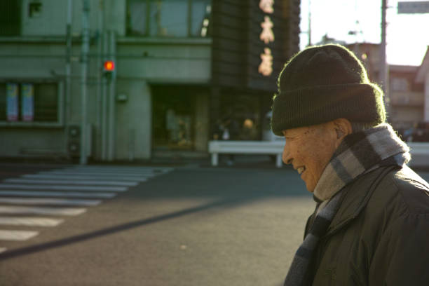 An old Asian man walking down the road in Winter wearing warm clothes