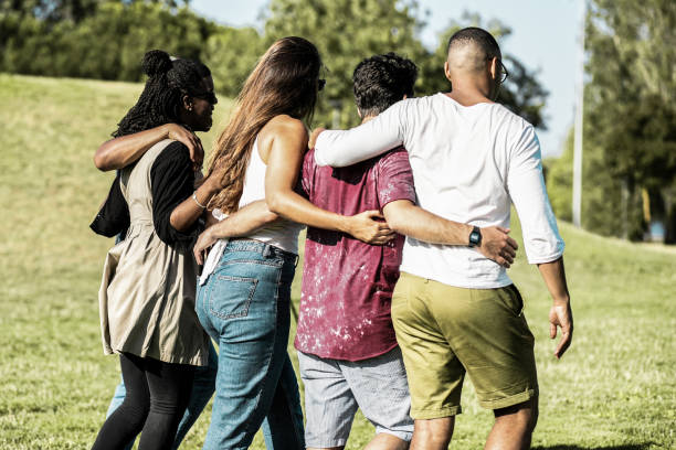 istock Back view of friends hugging while strolling on meadow. 1209806674