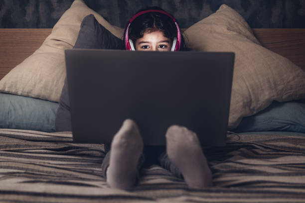 istock little girl sitting on the bed with a computer 1209808555