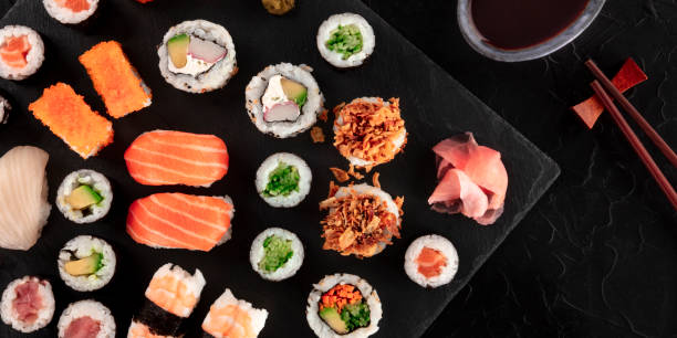 duży zestaw sushi panorama z sosem sojowym i pałeczkami, nakręcony z góry na czarnym tle. asortyment różnych maki, nigiri i rolek - sushi california roll salmon sashimi zdjęcia i obrazy z banku zdjęć
