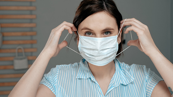Una chica atractiva se pone una máscara quirúrgica en su cara. Frío, gripe, virus, infecciones respiratorias agudas, cuarentena, epidemia, ironía, concepto de sarcasmo. De cerca photo