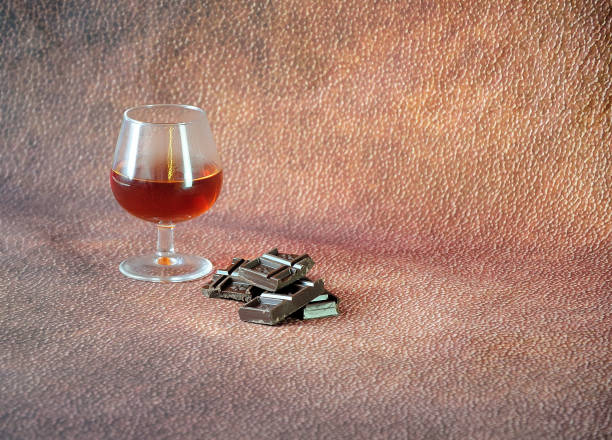 un verre de cognac et quelques morceaux de chocolat sur un fond abstrait brun. fermez-vous vers le haut. - brown chocolate candy bar close up photos et images de collection