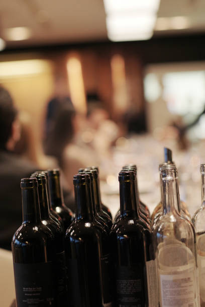 istock Black and white empty wine bottles on a table at the wine tasting evening event unrecognizable people at background 1209820071