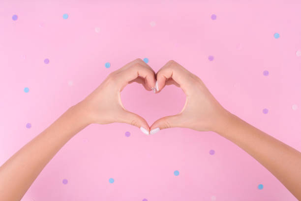 istock Young woman's hand with manicure making heart on pink background. 1209822334