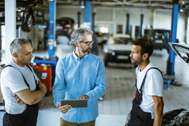 istock Mid adult manager using touchpad and talking to car mechanics in a workshop. 1209823077