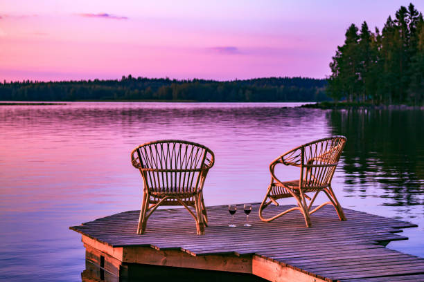 dos sillas de ratán y copas de vino tinto en un muelle con vistas a un lago al atardecer en finlandia - finland lake summer couple fotografías e imágenes de stock