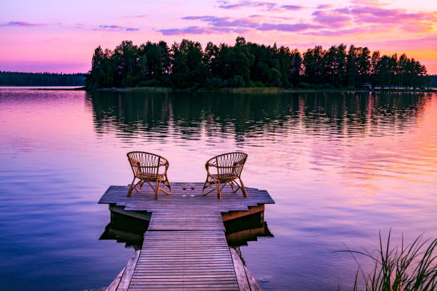 dos sillas de ratán y copas de vino tinto en un muelle con vistas a un lago al atardecer en finlandia - finland lake summer couple fotografías e imágenes de stock