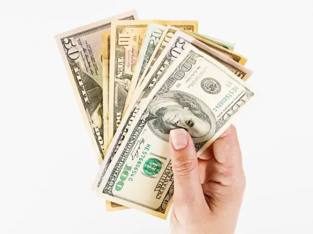 A woman's hand holds aloft a fanned-out selection of different denomination US banknotes.