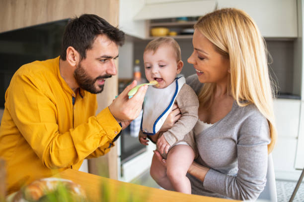 Father and mother feeding their little baby at home stock photo