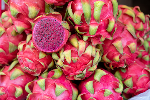 A cut dragonfruit on a pile of whole dragon fruits for sale at a market in India