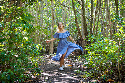 A young woman in a beautiful blue dress spins and dances on a wilderness trail in Fort Lauderdale, Florida.