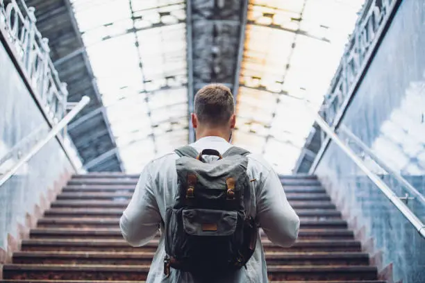 Photo of traveler man with backpack walking up by stairs