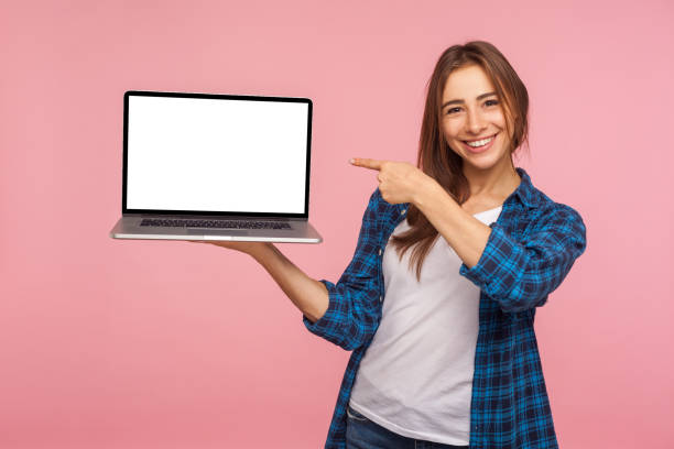 портрет счастливой очаровательной девушки в клетчатой рубашке, показывающей пустой экран ноутбука и улыбающуюся, указывая макет - holding laptop women computer стоковые фото и изображения