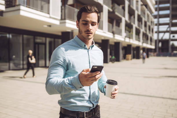 istock Young businessman using mobile phone while standing in city during sunny day 1209842821