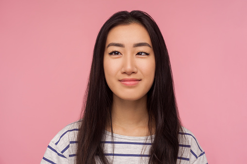 Closeup portrait of funny positive girl with brunette hair in striped t-shirt making silly face with crossed eyes and smiling, looking childish cute. indoor studio shot isolated on pink background