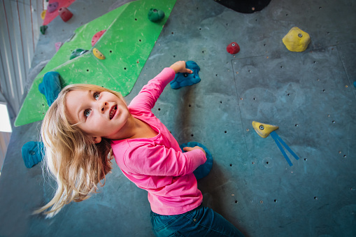 Cute small girl climbing on artificial boulders wall in gym, kids exercise