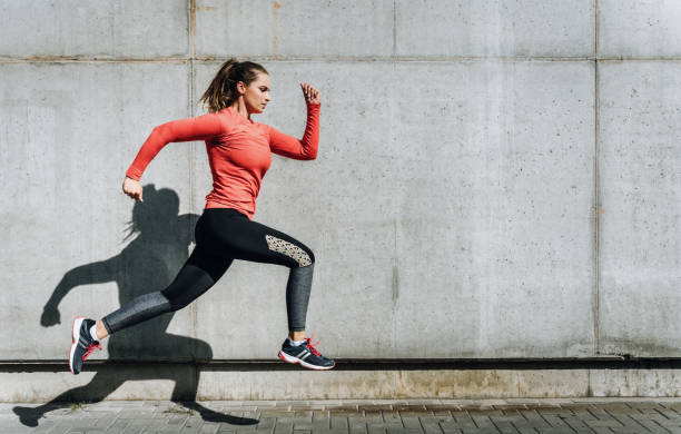 istock Side view of young woman running on footpath by wall 1209847218