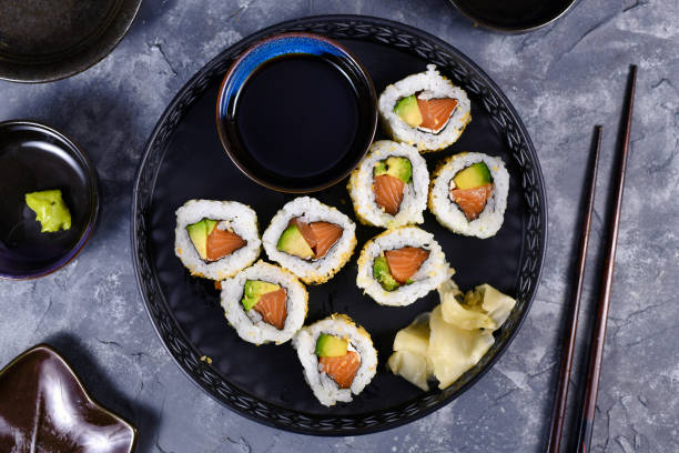 sushi california brötchen eingereicht rohen lachs fisch, avocado, frischkäse und mit sesam gekrönt - das innere nach außen gekehrt stock-fotos und bilder