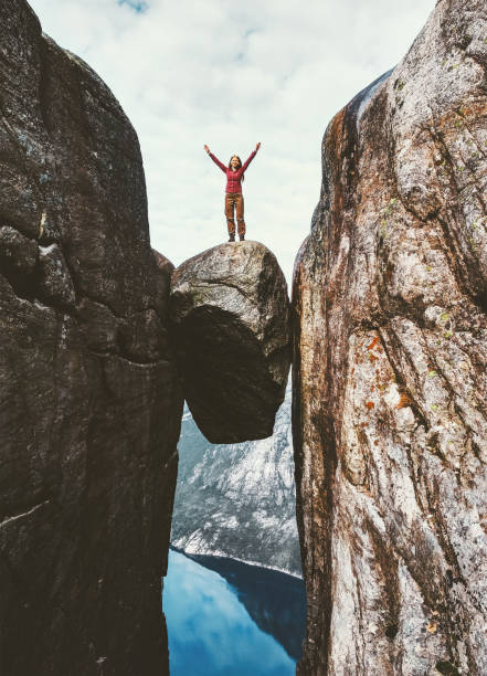 woman tourist on kjeragbolten raised hands travel in norway kjerag mountains extreme vacations adventure tourist happy emotions success concept - kjeragbolten imagens e fotografias de stock