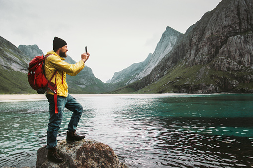 Tourist Man taking selfie by smartphone sightseeing Lofoten islands beach Travel lifestyle wanderlust concept adventure outdoor summer vacations