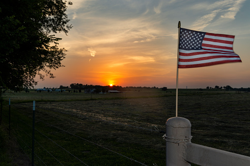 An American flag on the fence of a farm near the city of Commerce in the State of Oklahoma, at sunset, USA.