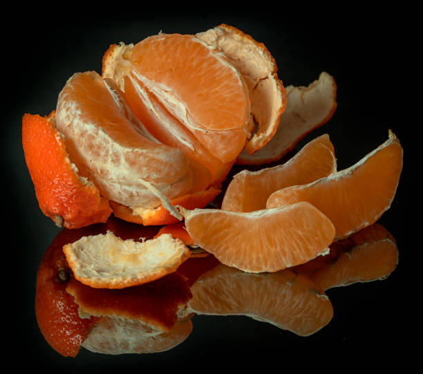 istock Half peeled mandarin on a black mirror surface with reflections isolated on black background. 1209855323