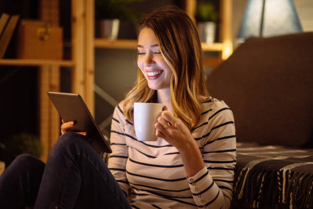 istock Young woman using digital tablet and drinking tea at night in her living room 1209862874