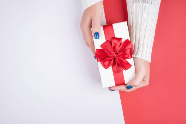 istock Gift box in women's hands on a gray red background 1209863124