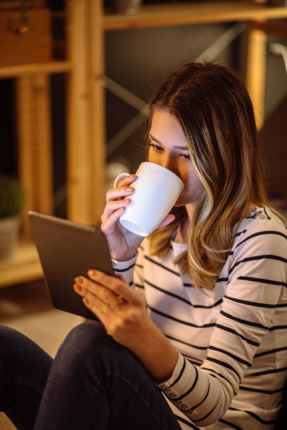 istock Young woman using digital tablet and drinking tea at night in her living room 1209863853