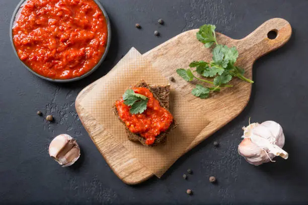 Tasty ajvar on toast. Vegetable sauce of baked red bell pepper on black. Balkan cuisine. Horizontal orientation. Top view.