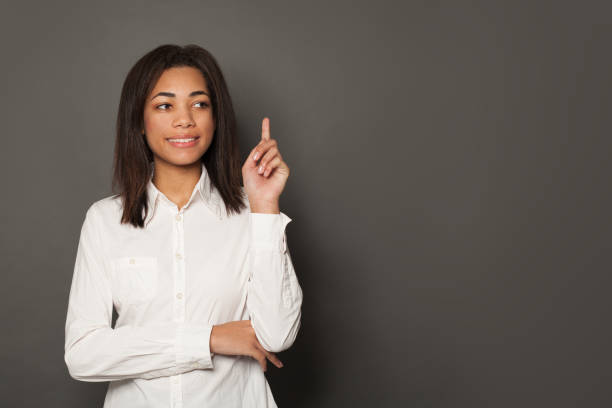 istock Black woman pointing up, smiling and looking aside on gray background 1209865547