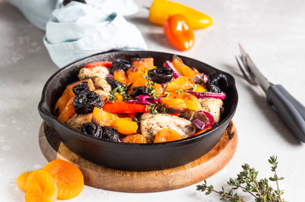 pollo alla griglia con verdure (peperone, carota e cipolla) e frutta secca (albicocche e prugne) in una padella di ghisa. sfondo grigio chiaro. copiare lo spazio. cibo sano. - antipasto roasted pepper bell pepper pepper foto e immagini stock