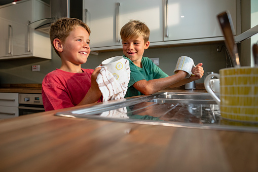 A side-view shot of two young brothers washing the dishes together.