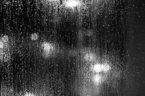 istock Black and white night light city behind glass windows rain water 1209868947