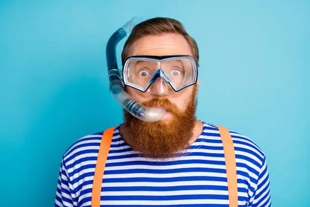 Close up photo of funky shocked red hair man watersport lover, breathe diving tube have mask wear nautical vest orange suspenders isolated over blue color background