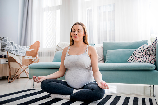 Meditating on maternity, pregnant woman meditating sitting on carpet at home