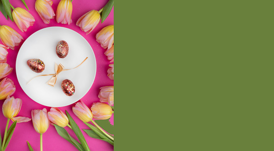 dinner white plate with luxury gold easter eggs, bow, beautiful tulip flowers frame Top view over pink table, easter concept, close up
