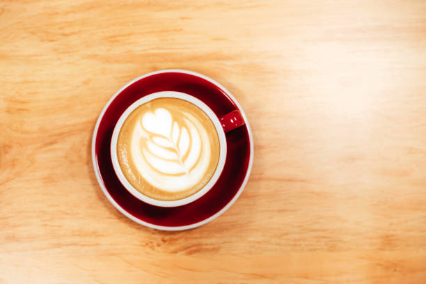 Cappuccino with frothy foam, red coffee cup top view closeup on wooden background. Flat lay style.